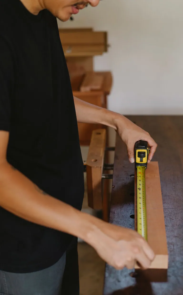 Craftsperson measuring a wood board at a workbench
